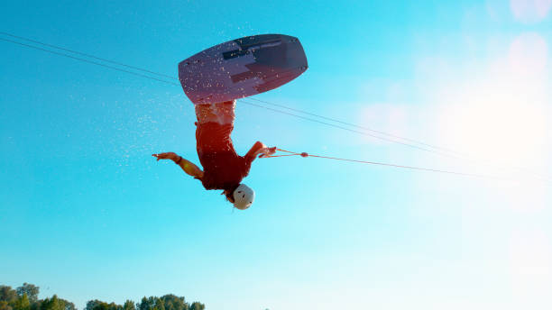 istock LENS FLARE: Extreme wakeboarder jumping and spinning across the clear blue sky. 1184004416