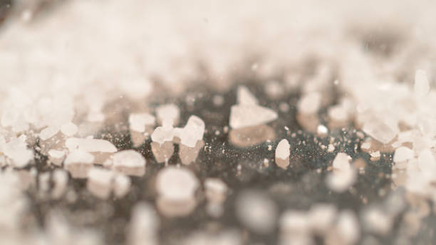 MACRO, DOF: Coarse white sugar is being sprinkled over the granite kitchen counter. Pristine white rock salt is scattered around the stone kitchen table. Sea salt is sprinkled over the black surface.