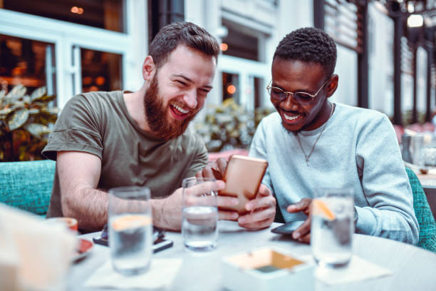hombre sueco riendo mientras navega por las redes sociales con su amigo africano - restaurant review fotografías e imágenes de stock