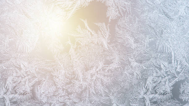 Unique frosty pattern on window glass. Soft sunlight shines through the window. Wide angle abstract natural background on winter holiday theme, banner format.