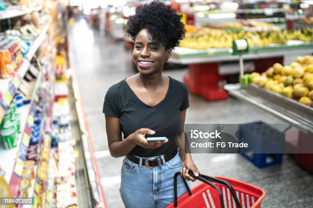 Giovane Donna Che Usa Il Cellulare E Sceglie Il Prodotto Al Supermercato - Fotografie stock e altre immagini di Supermercato