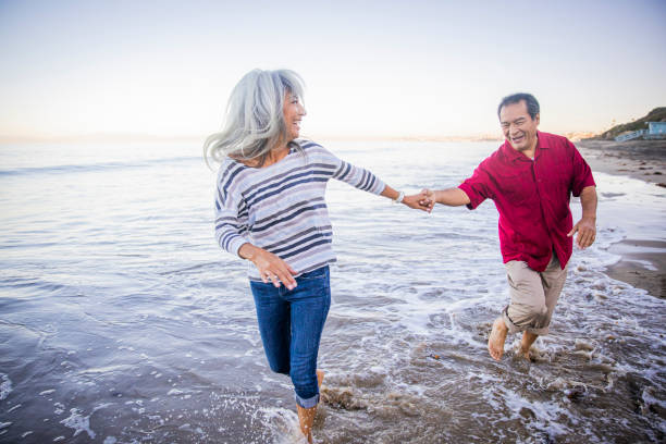해변을 따라 걷는 수석 히스패닉 커플 - running cheerful outdoors senior couple 뉴스 사진 이미지