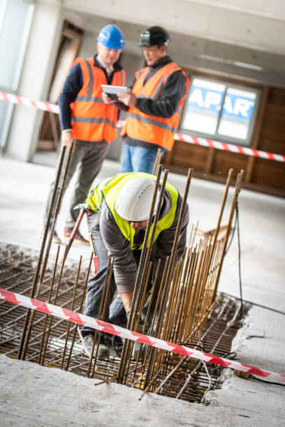 istock Construction worker cutting iron mesh while two men look at a digital tablet in the background 1184015417