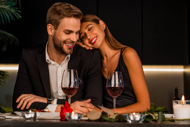 ワインとキャンドルで特別なイベントを祝う興奮した愛情のあるカップル、一緒に夕食を食べる - feast day 写真 ストックフォトと画像