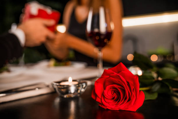 istock Young man giving his girlfriend gift box for present. focus on rose and candle on foreground 1184016204