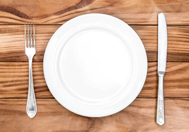 istock Empty plate with fork and knife on the brown wooden table. Top view. 1184016820