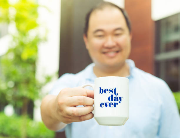 Asian man holds a cup or mug that says 
