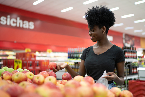 Young woman choosing apple in supermarket