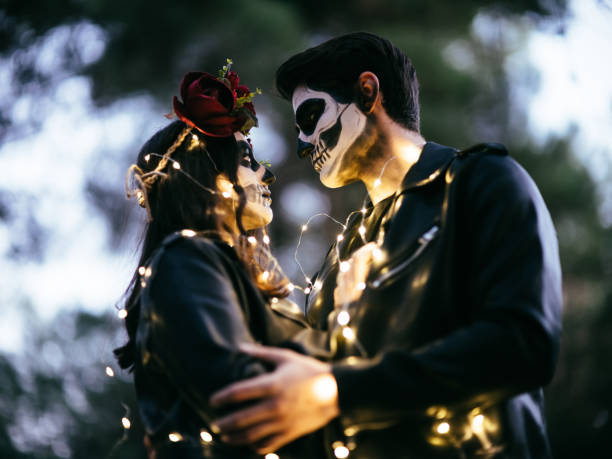 Halloween loving couple in costumes of skeletons and sugar skull makeup on forest stock photo