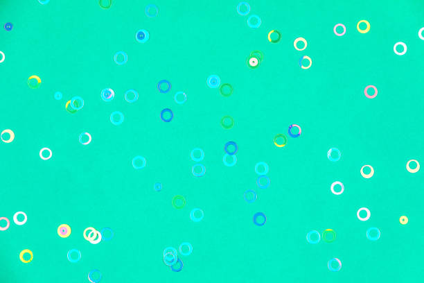 Colorful holographic foil confetti background. Pastel colored pink, blue and yellow circles sparse on trendy mint green colored paper. Simple holiday concept. Top view, flat lay