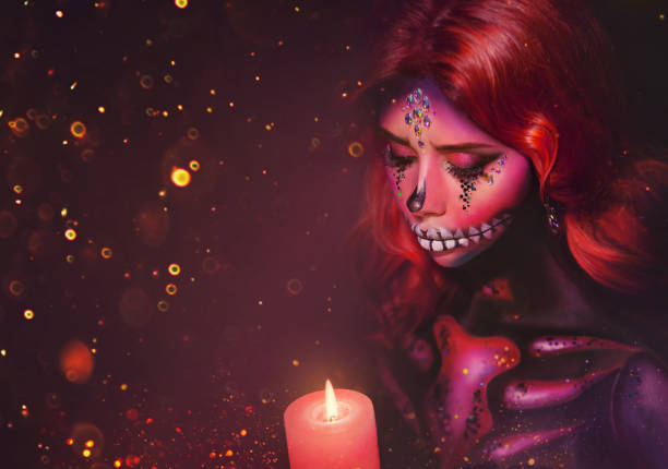 istock woman with creative multi-colored makeup sugar skull with stones and slices, holding a burning candle in her hands. greasepaint body art, aqua paints. Free space for text. Celebrate Dia de los Muertos 1184029932
