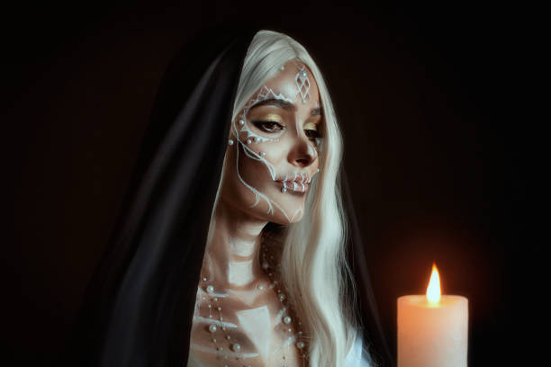 a woman in the image of an attractive mysterious witch with white ashy hair holds a burning candle. creative makeup for halloween party. black poppy and dark backdrop. celebrating dia de los muertos - witch beauty beautiful women imagens e fotografias de stock