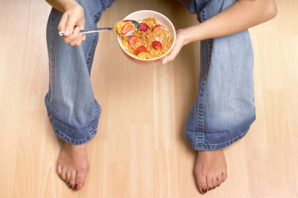 istock Young woman sat on the floor eating breakfast cereal 1184032262