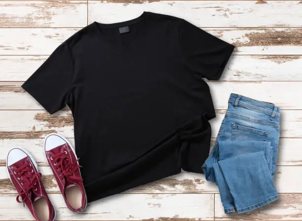Photo of Mockup of blank black t shirt and jeans jacket, red sneakers and denim pants on white wooden background. Shirt design for man. Flat lay, top view.
