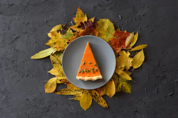 Delicious pumpkin pie piece with autumn leaves on black background top view copy space. Thanksgiving or harvest concept overhead view