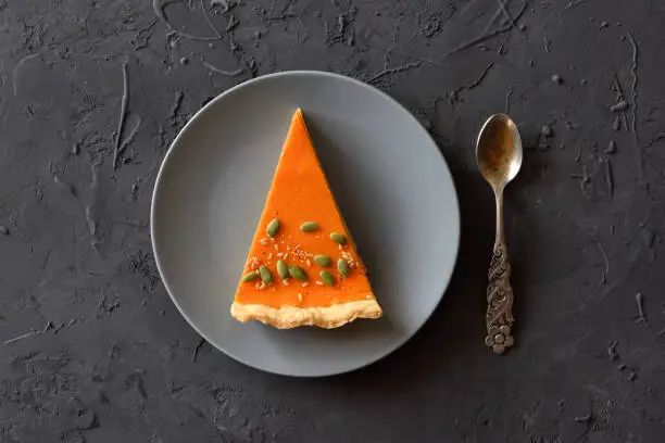 Piece of traditional pumpkin pie with seeds on black background. Minimalist Thanksgiving dessert concept overhead view