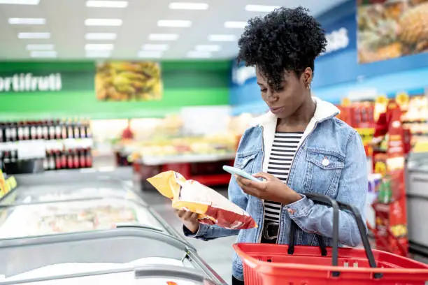 Woman is shopping in supermarket and scanning barcode with smartphone