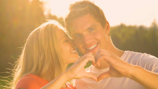 istock PORTRAIT: Happy man looks at camera while making a heart symbol with girlfriend 1184048383