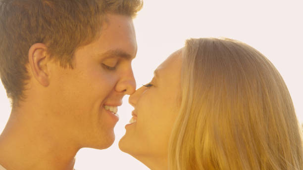 CLOSE UP: Bright sun rays shine on man giving his girlfriend an eskimo kiss. CLOSE UP: Bright sun rays shine on the handsome young man giving his girlfriend an adorable eskimo kiss. Young Caucasian newlyweds kissing in the nature on a beautiful summer day in the countryside. joined at hip stock pictures, royalty-free photos & images