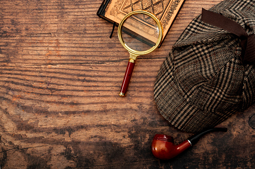 Literary fiction, investigate crime and mystery story conceptual idea with sherlock holmes detective hat, smoking pipe, retro magnifying glass and old book isolated on wood table top with copy space