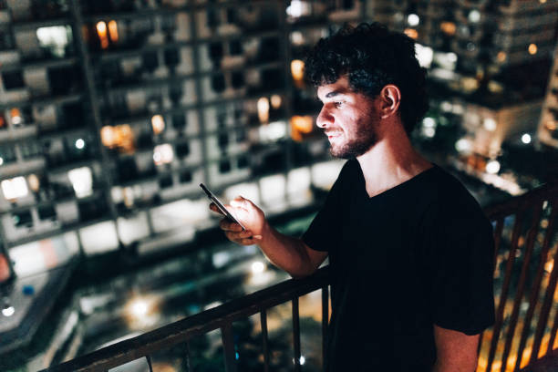 istock Young man using smartphone on residential balcony at night 1184080551
