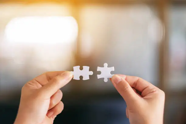 Closeup image of two hands holding and putting a piece of white jigsaw puzzle together