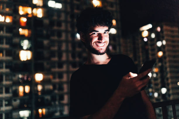 istock Young man using smartphone on residential balcony at night 1184082909
