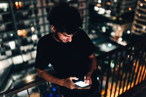 istock Young man using smartphone on residential balcony at night 1184082941