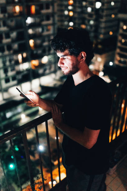 istock Young man using smartphone on residential balcony at night 1184082990