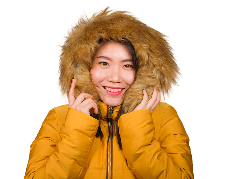 winter fashion isolated portrait of young beautiful and happy Asian Korean woman in warm yellow feather jacket with fur hood gesturing cheerful and playful smiling with sweet face expression