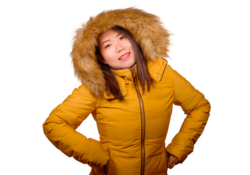 winter fashion isolated portrait of young beautiful and happy Asian Chinese woman in warm yellow feather jacket with fur hood gesturing cheerful and playful smiling with sweet face expression