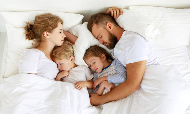 gezonde slaap. gelukkige familie ouders en kinderen slapen in een wit bed - kussen beddengoed stockfoto's en -beelden