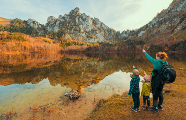 mamá y los niños en la orilla del laudachsee, austria, con el impresionante katzenstein subiendo en el fondo y reflexionando en el agua cristalina - indiana summer lake tree fotografías e imágenes de stock