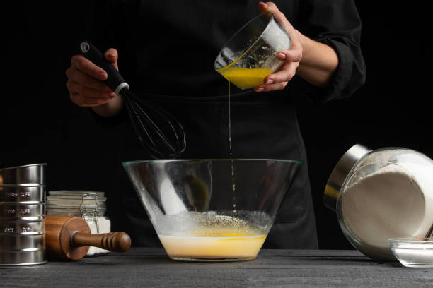 istock a pastry chef or baker cooks dough, pours yeast into a container, for making sweets, rolls or Italian pizza or pasta. Freezes in motion. On a black background, horizontal photo 1184114625