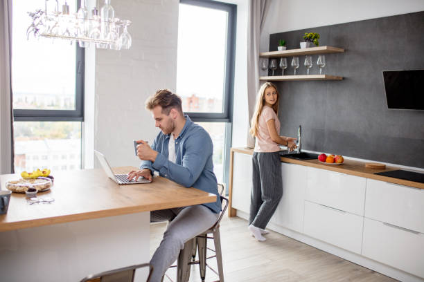 istock gorgeous woman cleaning the kitchen while her husband surfing the net 1184132510