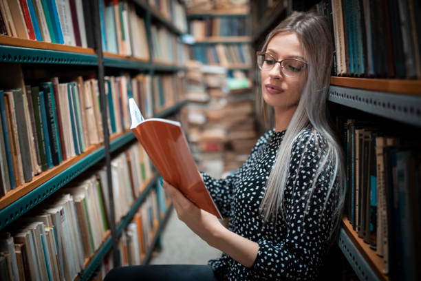 istock Young female student read and learns by the book shelf at the library 1184133507