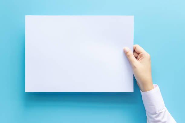 istock close up hands holding empty white blank letter paper size A4 for flyer or invitation mock up isolated on a blue background. 1184134111