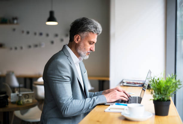 istock Mature man with laptop at the table in a cafe, working. 1184141503