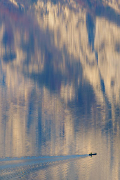 Man rowing in a small canoe on a calm alpine lake reflecting mountains