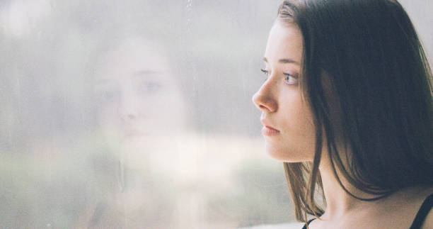 istock Pensive girl looks out the window 1184154099
