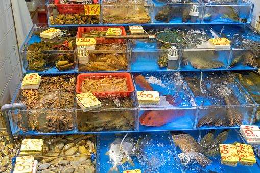 A seafood vendor in the Makishi Market in Okinawa, Japan. The vendor has a water tank with live lobsters and a shelf with various fresh seafood such as fish, shellfish, and sashimi.