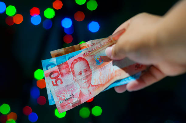 A hand giving many cash of Philippines peso currency in Christmas holiday. Close up shot handing out or giving money as a gift or as a payment in Christmas holiday background. philippines currency stock pictures, royalty-free photos & images