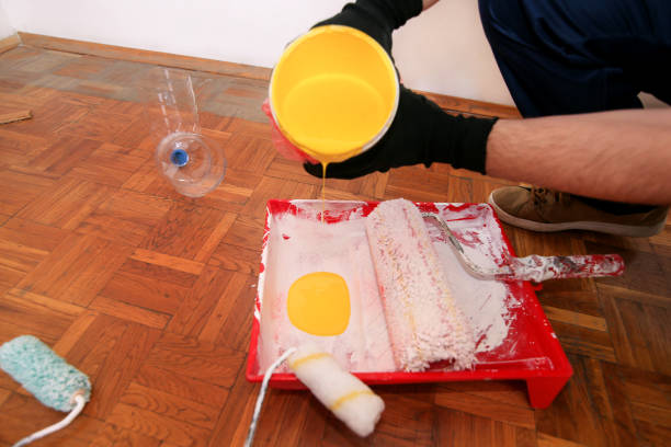 istock Construction worker and handyman doing finish renovation at apartment. Professional painter with black gloves pours yellow color from bucket into red bowl for paint mixing. Home renovation concept. 1184168078