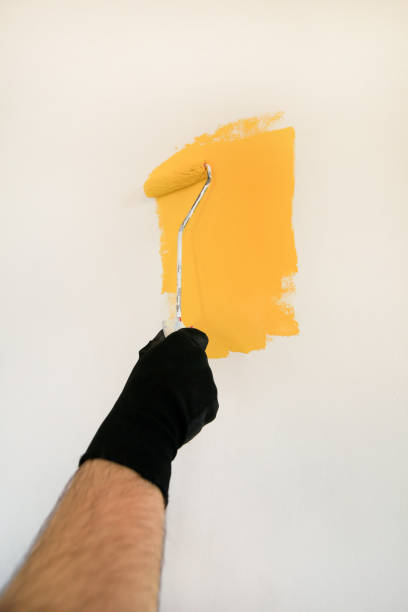 istock Construction worker and handyman doing finish renovation at apartment. Professional painter using paint roller brush painting of wall with yellow color on construction site. Home renovation concept. 1184168252