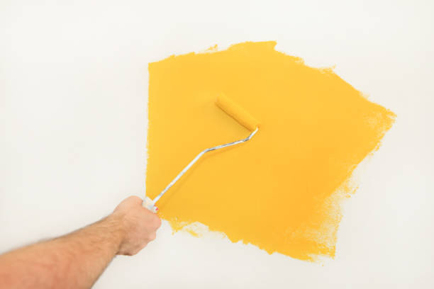 istock Construction worker and handyman doing finish renovation at apartment. Professional painter using paint roller brush painting of wall with yellow color on construction site. Home renovation concept. 1184168318