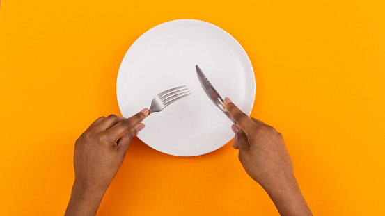 Restaurant and Food Concept. Black female hands cutting invisible object on empty plate over orange background