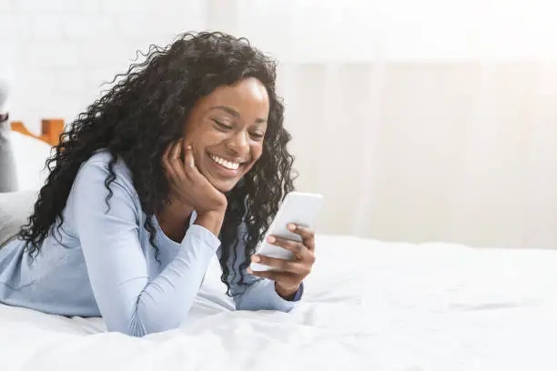 Photo of Black girl in love reading messages from her boyfriend