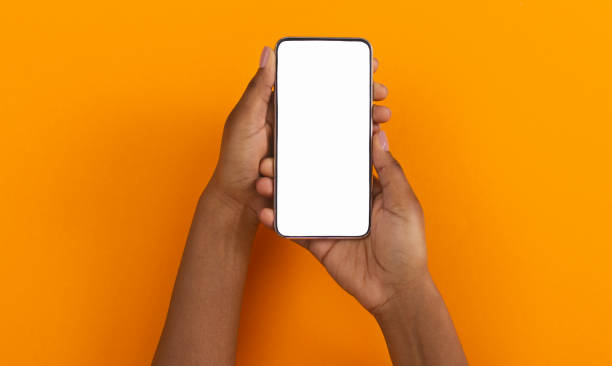 Black hands holding smartphone with blank screen for mockup Modern smartphone with blank screen for mockup in african american woman's hands on orange background, top view with free space hand holding phone stock pictures, royalty-free photos & images