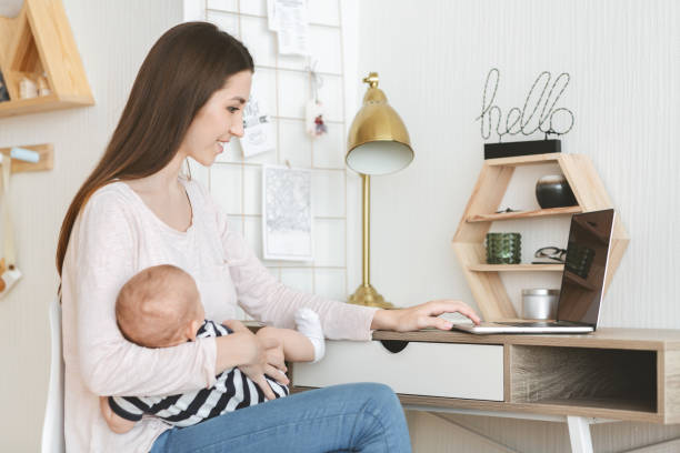 istock Woman using laptop while holding her child in arms 1184172627