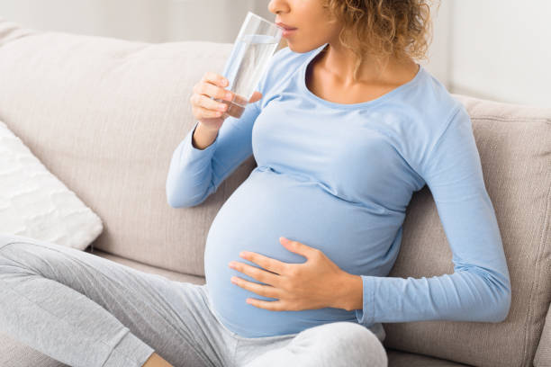 istock Pregnant woman drinking water sitting on sofa 1184172678